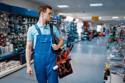 制服的男性工作者在工具商店拿着工具箱在五金店中选择专业设备穿制服的男工人在工具存储区中持有工具箱